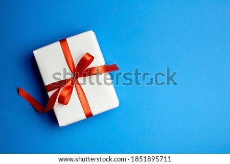 White gift box tied with red ribbon on blue background