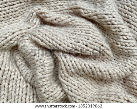 Knitted woolen fabric texture for background.  Natural knitted soft wool of light beige color close-up.  Top view, copy space, flat lay.