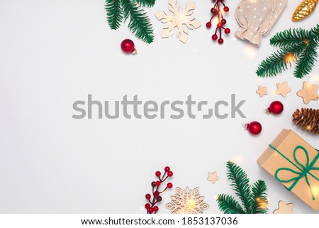 Christmas frame with present in craft paper, decorations, pine cones, berries, fir tree branches on white background with lights. Flay lay, copy space