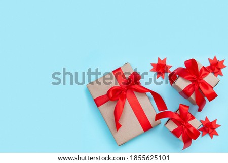 Three gift boxes with a red bow and origami paper stars on a pastel blue background. Minimal festive composition. Copy space for text.