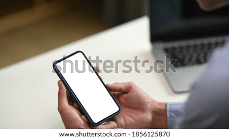 Cropped shot of professional businessman holding blank screen smartphone in modern office room.