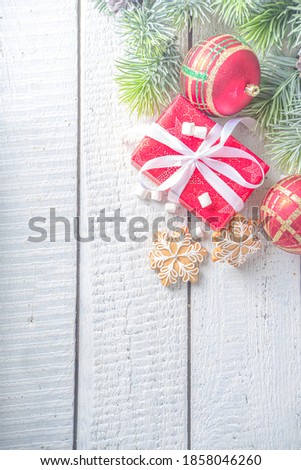 Christmas fir branches, gift boxes with festive ribbon, Christmas decoration, gingerbread cookies and baubles on white wooden background. Xmas and New Year greeting card, winter holiday.