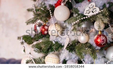 Decorated Christmas tree in the room. Coniferous tree with white and red baubles located near the white wall during the celebration of the holiday
