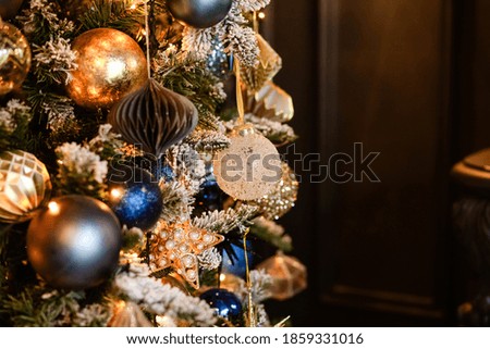 A beautiful elegant Christmas tree is decorated for the holiday with yellow,gold, shiny balls and toys at home on a dark blue background.Romantic evening.Merry Christmas!Happy New Year!Copy space