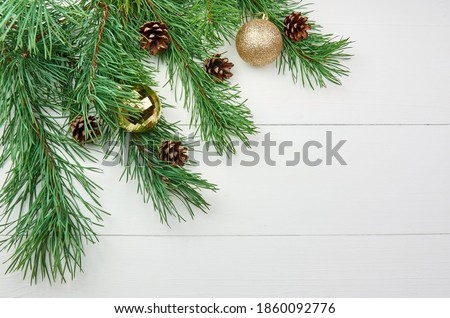 Green pine tree branches with cones and christmas decorations on white wooden background