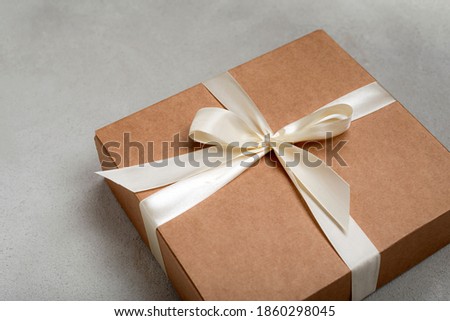 Craft colored christmas gift box with white ribbon on gray background