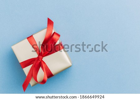 A single present wrapped in golden wrapping paper with a red ribbon bow sitting on a blue background