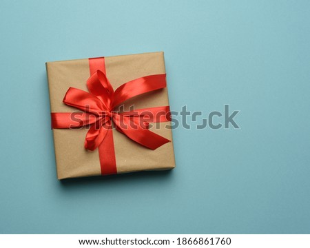 box wrapped in brown paper and tied with a red silk ribbon with a bow, gift on a blue background, top view, copy space