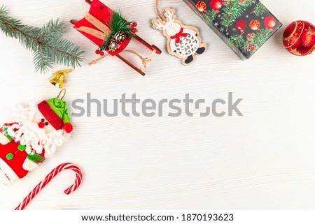 toy sleigh of santa claus, figurine of a deer, christmas tree branch, cones, bell, toy santa claus and lollipop staff on a background of white wood with gold veins