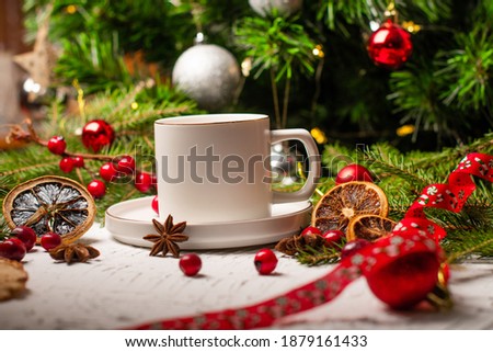 New Year's drink in a white cup on the background of a Christmas tree. Cranberry, dried orange, star anise, and cinnamon stick