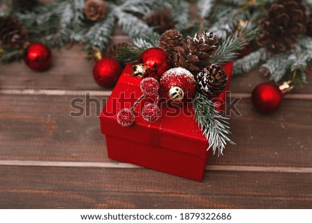 red celebratory winter box with handmade decor on wooden old table with fir branches, pine cones and toys