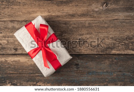 Beige gift box tied with a red ribbon on a wooden background. Top view, with space to copy. The concept of holiday backgrounds.