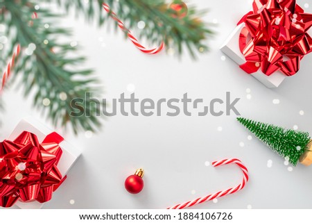 Christmas decoration red background. White gifts with scarlet bow, red balls and sparkling lights in xmas decoration on white background for greeting card. Flat lay, top view, copy space