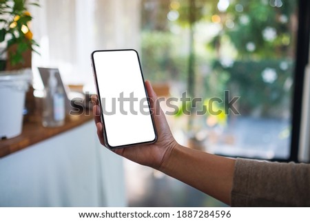 Mockup image of a woman holding mobile phone with blank white desktop screen