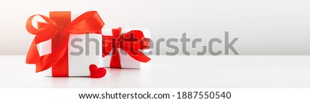 Gift box with red bow ribbon and red paper heart on white table for Valentines day with copyspace.
