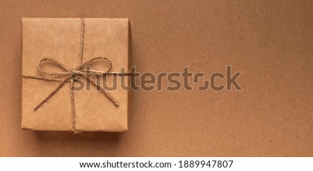 Gift box wrapped in craft paper with jute bow on kraft eco background with copy space.