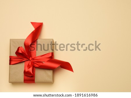 square gift box is packed in red paper and curled silk ribbon, festive background, top view 
