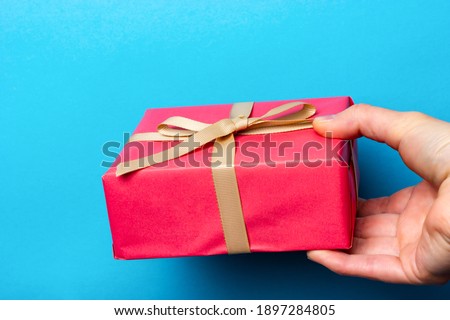 A woman's hand holds out a pink gift box with a beige ribbon. Gift giving process.