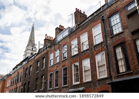 Very typical London street with brick wall houses and a church tower on the background