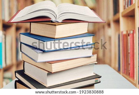 A stack of books on a wood table. Library in the background.