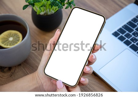 female hand holding golden phone with isolated screen on wooden table in office 