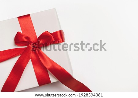 White gift box with red ribbon bow on light background. Christmas, new year, birthday, anniversary or sale background. Top view, flat lay, copy space, template for design