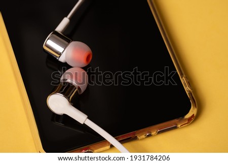 Phone on a yellow background. There are white headphones on the phone. Close-up.