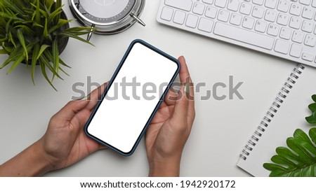 Mock up image of young woman holding smart phone with blank screen on white desk.