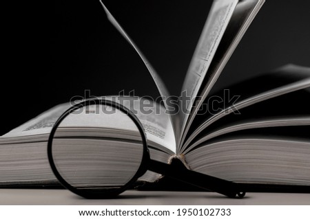 Open book close up with turning pages and magnifying glass. Textbook in hardcover on desk. Education and research concept.