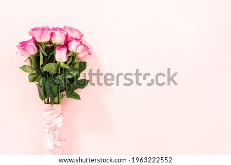 Bouquet of pink roses wrapped in pink wrapping paper with a pink ribbon on a pink background.