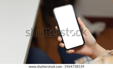 Over shoulder close up view of female hand holding smartphone with mock-up screen at workplace, clipping path