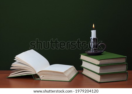 open blank book and stack of books with burning candles on green background