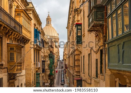 Typical narrow street of Valletta with Cathedral dome, yellow buildings and colorful balconies, Malta, Europe. Travel destination