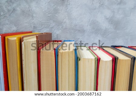 Row of multicolored hardback books on wooden table against gray and blue concrete wall
