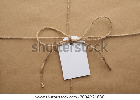 Parcel wrapped in kraft paper with tag as background, closeup