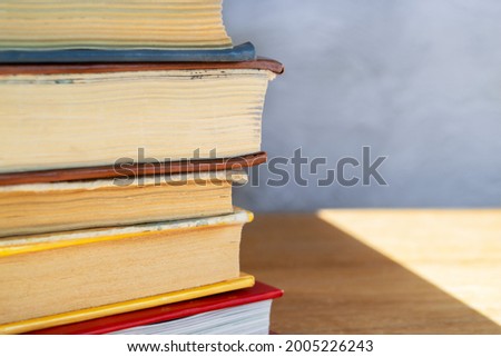 Stack of colorful hardback books on wooden table close up against gray and blue concrete wall