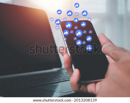 The concept with notification icons of like above smartphone screen, Social media interactions on mobile phone, a man's left hand holding device, internet digital marketing.