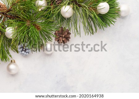 A pine branch with cones is decorated with shiny Christmas balls. Simple white background. A beautiful frame for your New Year and Christmas greetings. High angle view.