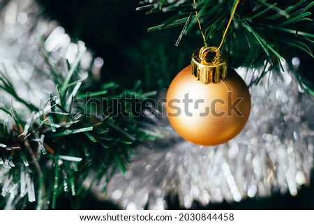 Golden ball on decorated Christmas tree with silver tinsel garland. Selective focus. Holiday card with decorations for the New Year's Eve