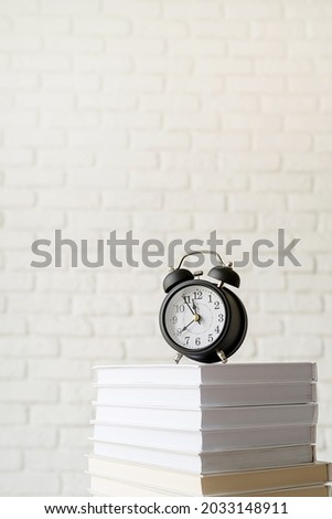  Back to school. Black alarm clock on stack of books on white brick wall background, copy space