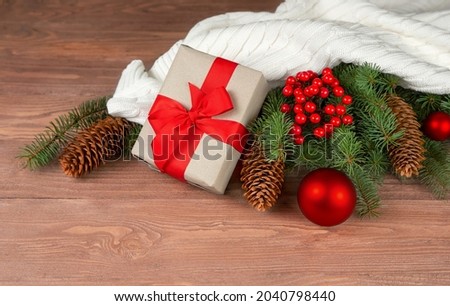 Christmas composition fir branches, cones, red balls, white knitted plaid, gift box on a wooden background.