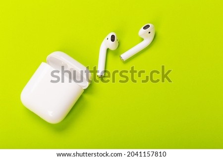 modern white wireless earphones with charging case on green background