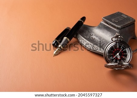 Fountain pen, beautiful details of a beautiful fountain pen, an antique ink holder and a beautiful pocket watch placed on caramel leather, selective focus.