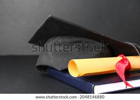 Graduation hat, diploma and book on dark background