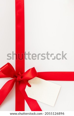 Christmas gift, red ribbon bow and empty note card on white background. Blank paper tag, copy space, greeting message template. New year holiday  present wrap decoration.