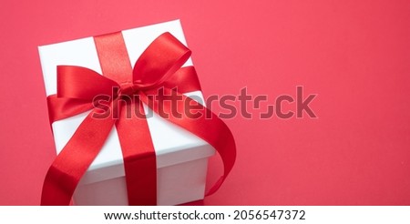 Christmas white gift box tied bow with ribbon on red color background, Valentine surprise, New Year holiday present, satin curly decoration. Copy space, greeting card template