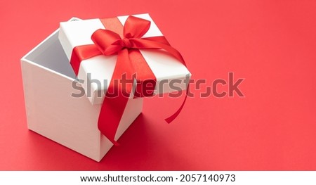 Christmas gift box white with red ribbon bow open on red color background, Valentine surprise, New Year holiday present, satin curly decoration. Copy space, greeting card template