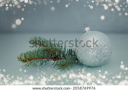 A Christmas tree toy lies on a blue background next to a fir branch.