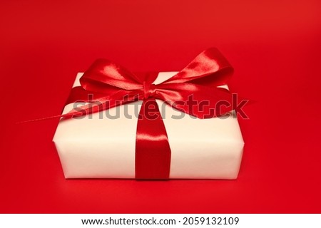 A gift box with big red bow against red background. Holidays concept