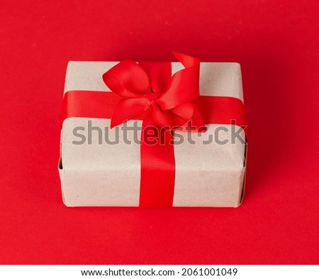 Gift box in craft paper on a red background with a red bow.